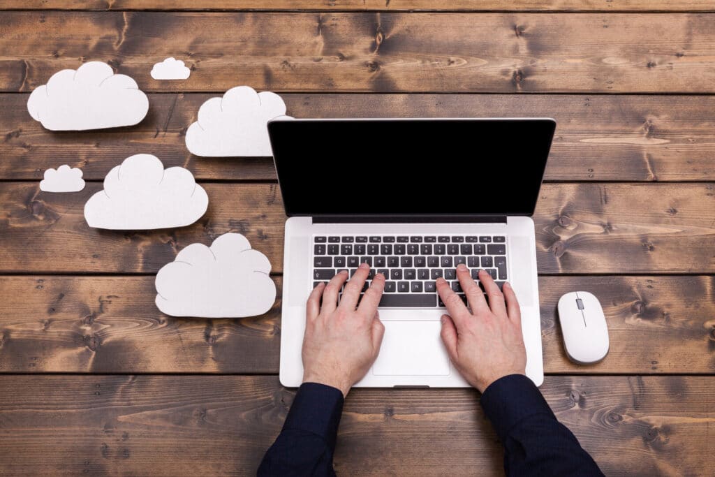 Schreibtisch holz mit Laptop Wolken und Cloud, hybride IT, hybride IT-Infrastruktur, IT in der Cloud, Cloud IT